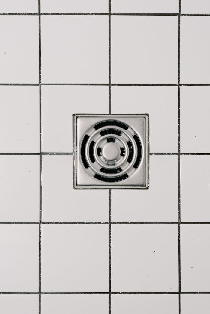 services-02 Top view of white ceramic tile floor with stainless steel square shaped cover of drain in contemporary shower