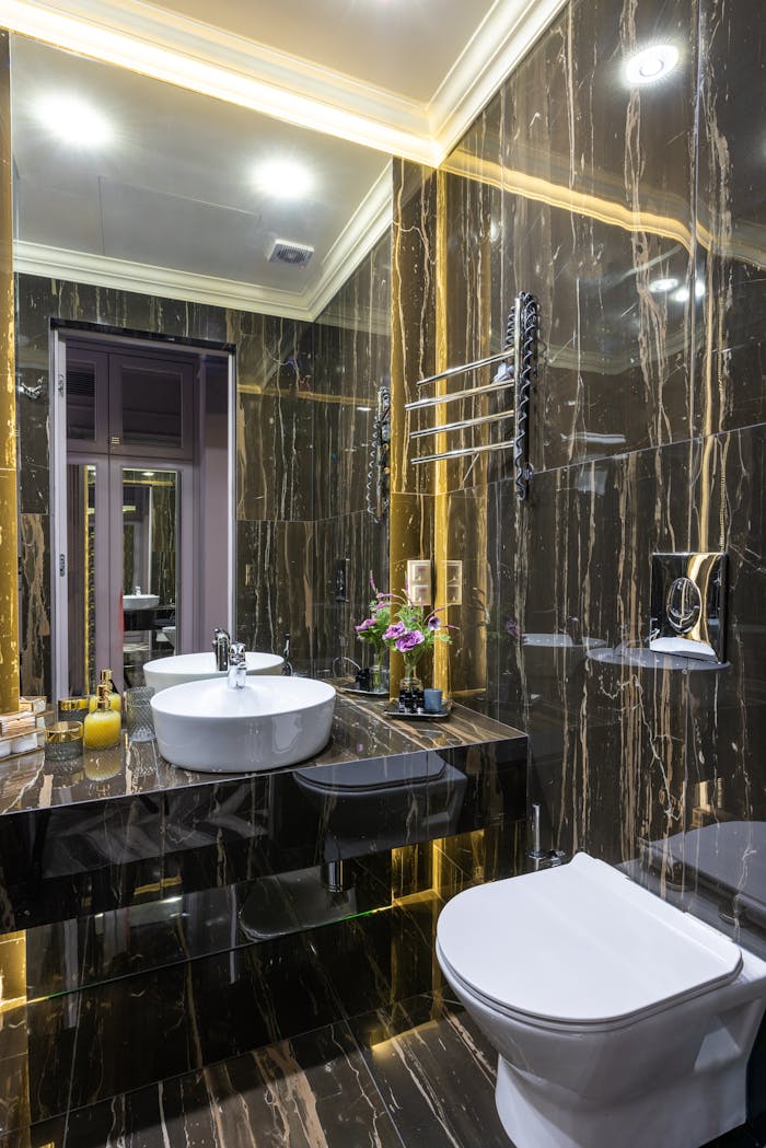 services-01 Contemporary bathroom with toilet bowl and washbasin reflecting in mirror under glowing lights in house